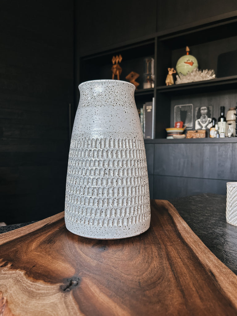 A stoneware carafe vase with a creamy white glaze, speckled detail and intricate carving.