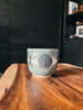 A handcrafted green ceramic cup featuring a sketched eye motif by artist Matthew Ward.