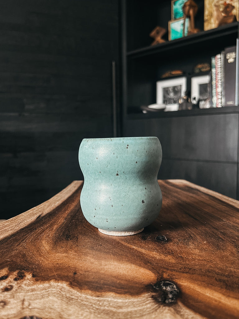 A handmade 'Laos' mug featuring a unique bubbly shape, in a teal color with speckled details and a smooth matte finish.