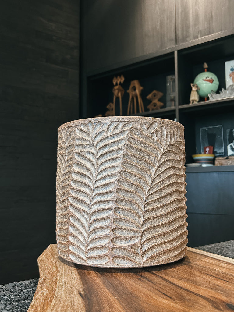A tan ceramic planter with a raised fern leaf pattern and matte textured finish.