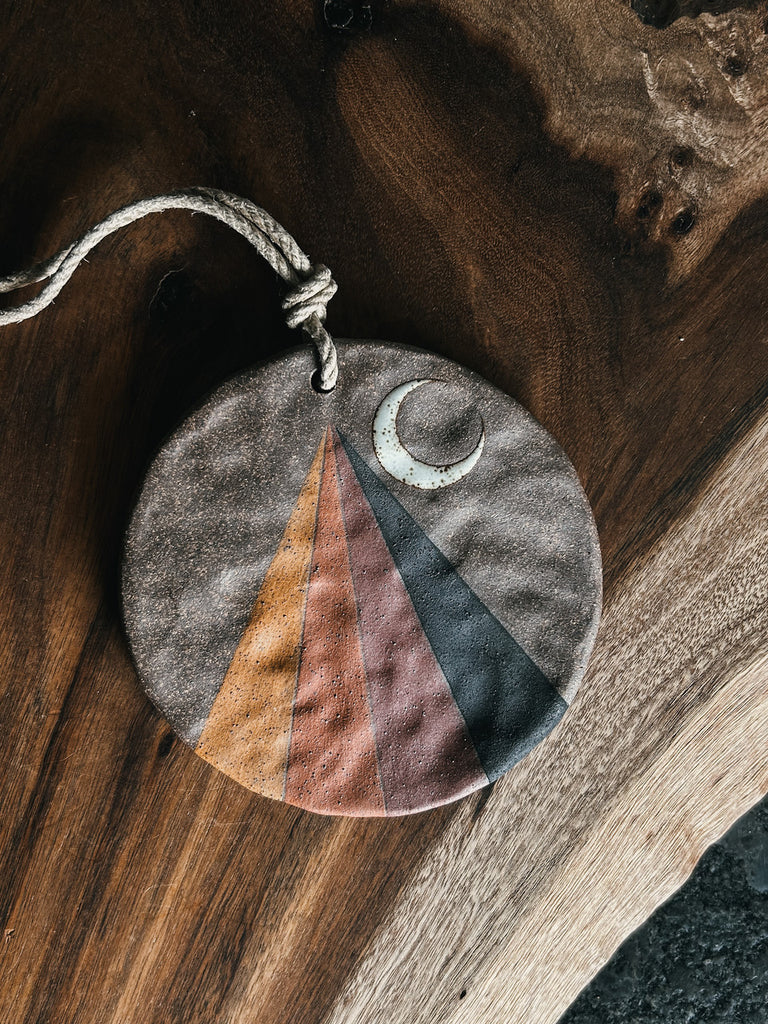 A round stoneware ornament featuring a rainbow prism.