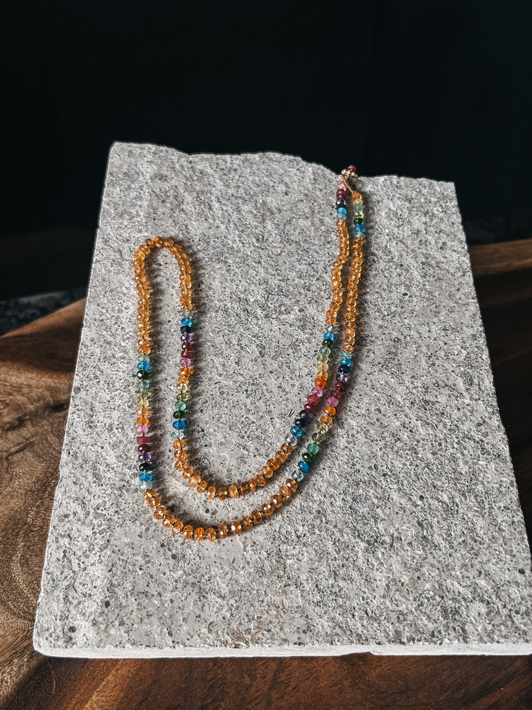 A handcrafted Amalia lei necklace featuring bright orange Spessartite garnets and rainbow gemstones.