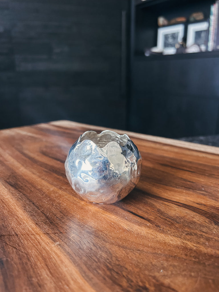 A small rounded sterling silver vessel with a hammered texture and scalloped opening.